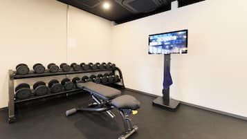 Un gimnasio con una banca, mancuernas y una pantalla de televisión que muestra 'TECHNOGYM'.