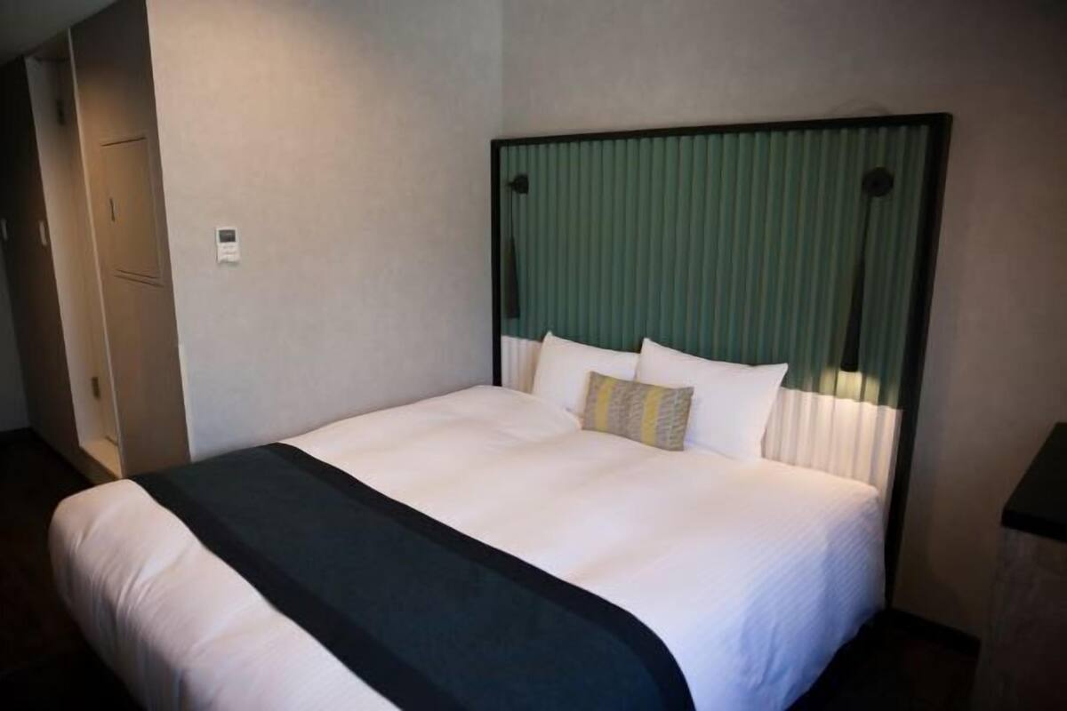 A hotel room with a large bed, a headboard with vertical blinds, a bedside table, and a wardrobe.