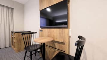 Une chambre d’hôtel compacte dotée d’une kitchenette, d’un coin repas avec une table et des chaises, et d’un grand téléviseur à écran plat fixé au-dessus du comptoir.