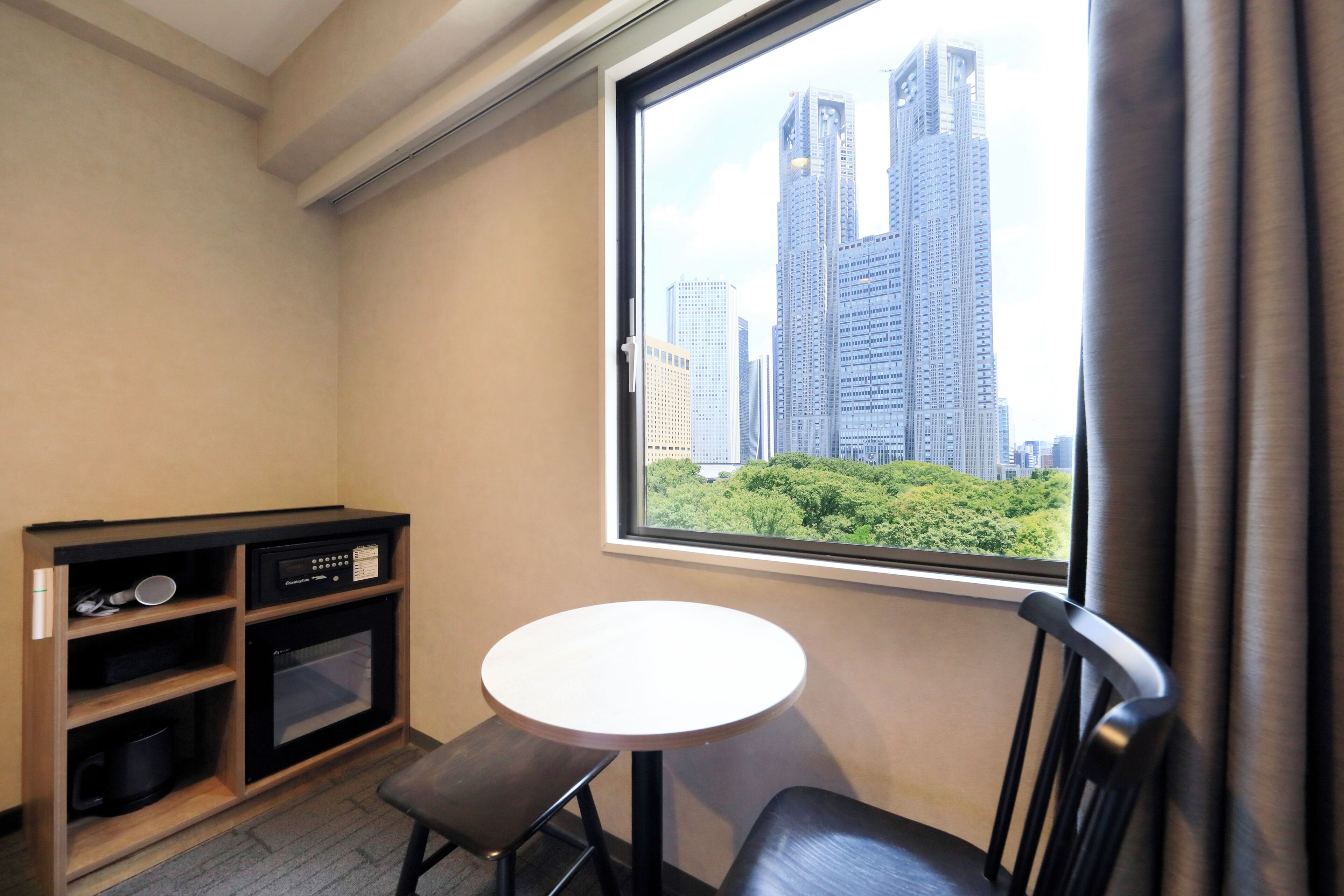 A small room with a window overlooking a cityscape, a kitchenette, and a single chair.