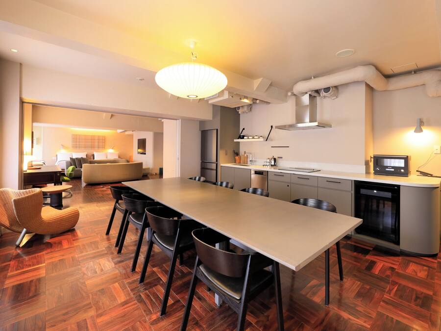 A modern kitchen with a long dining table, chairs, and a built-in oven.