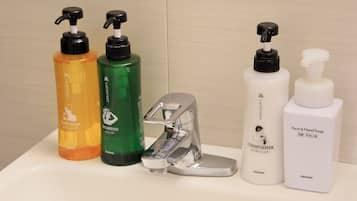 A bathroom counter with various toiletries including body soap, shampoo, conditioner, and face & hand soap.