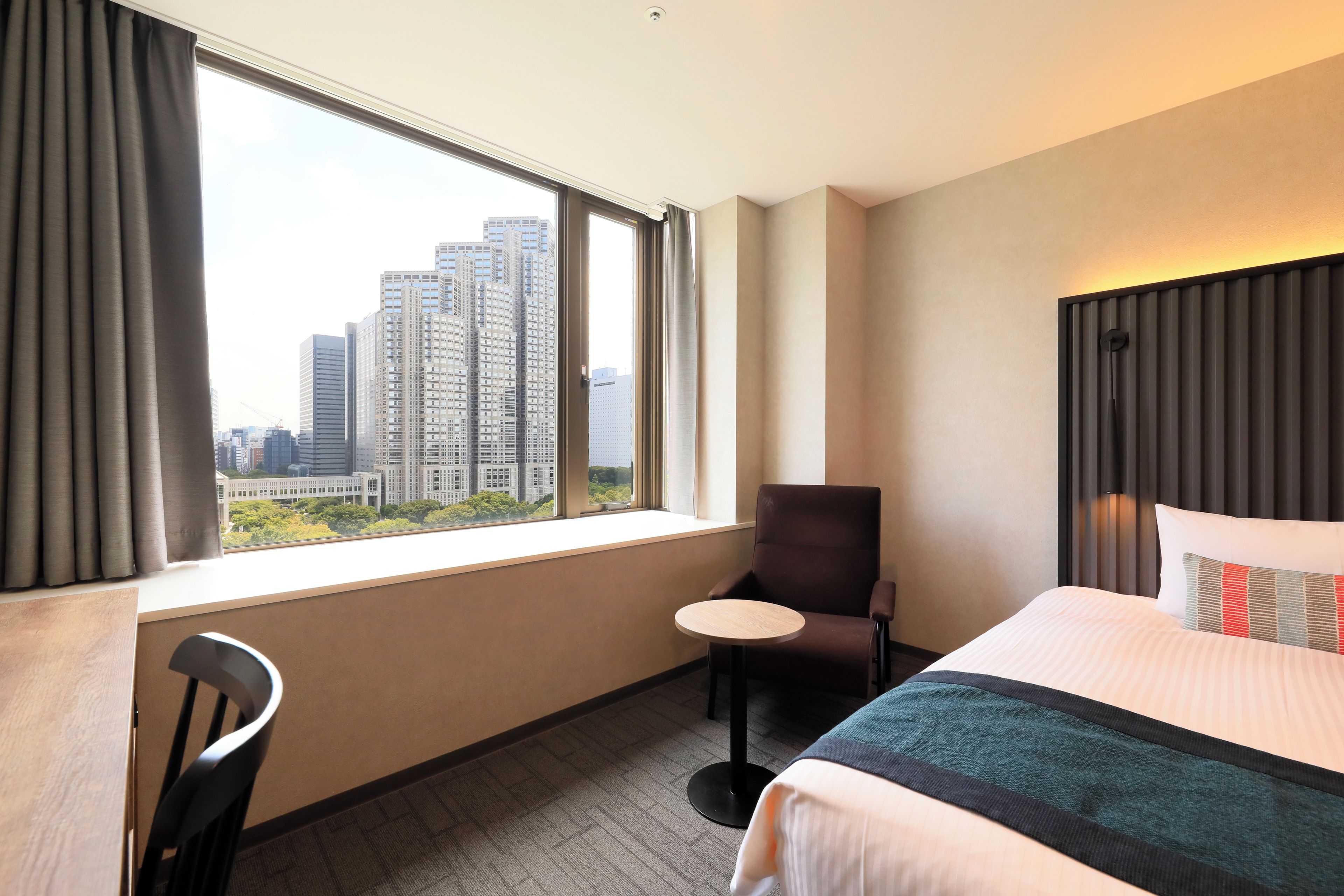 A hotel room with a large window, a bed, a chair, and a small table.