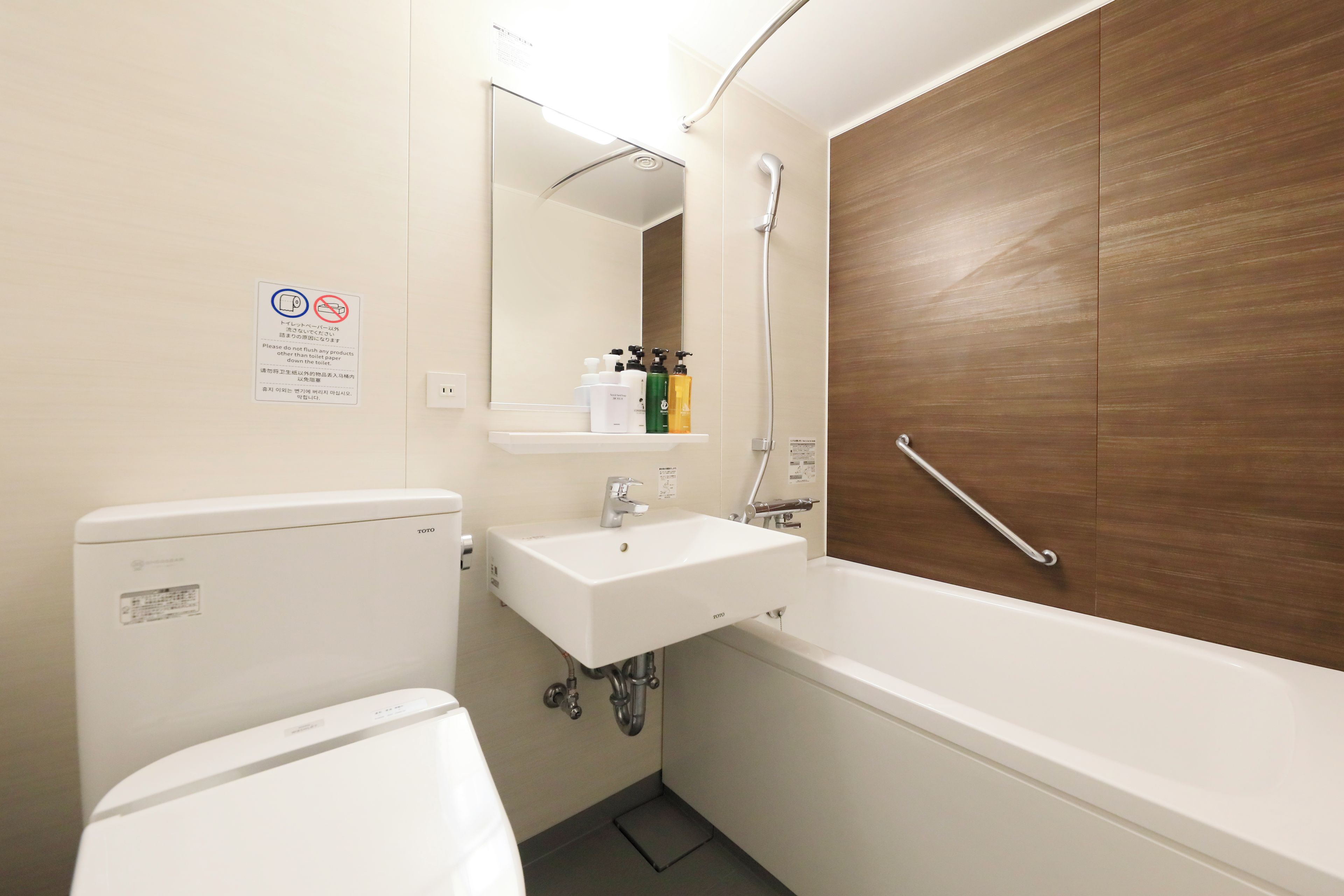 A bathroom with a toilet, sink, and bathtub. There is a mirror above the sink and a wooden panel on the wall.