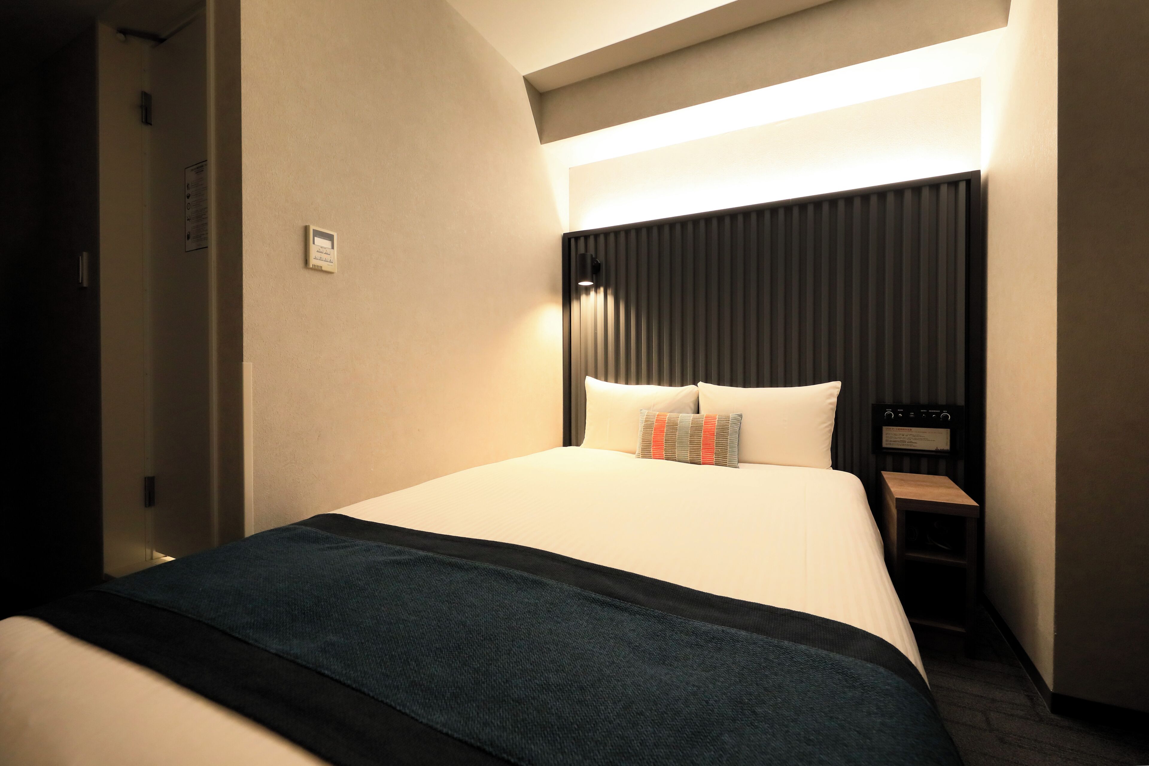 A hotel room with a large bed, a bedside table, a lamp, and a wall-mounted control panel.