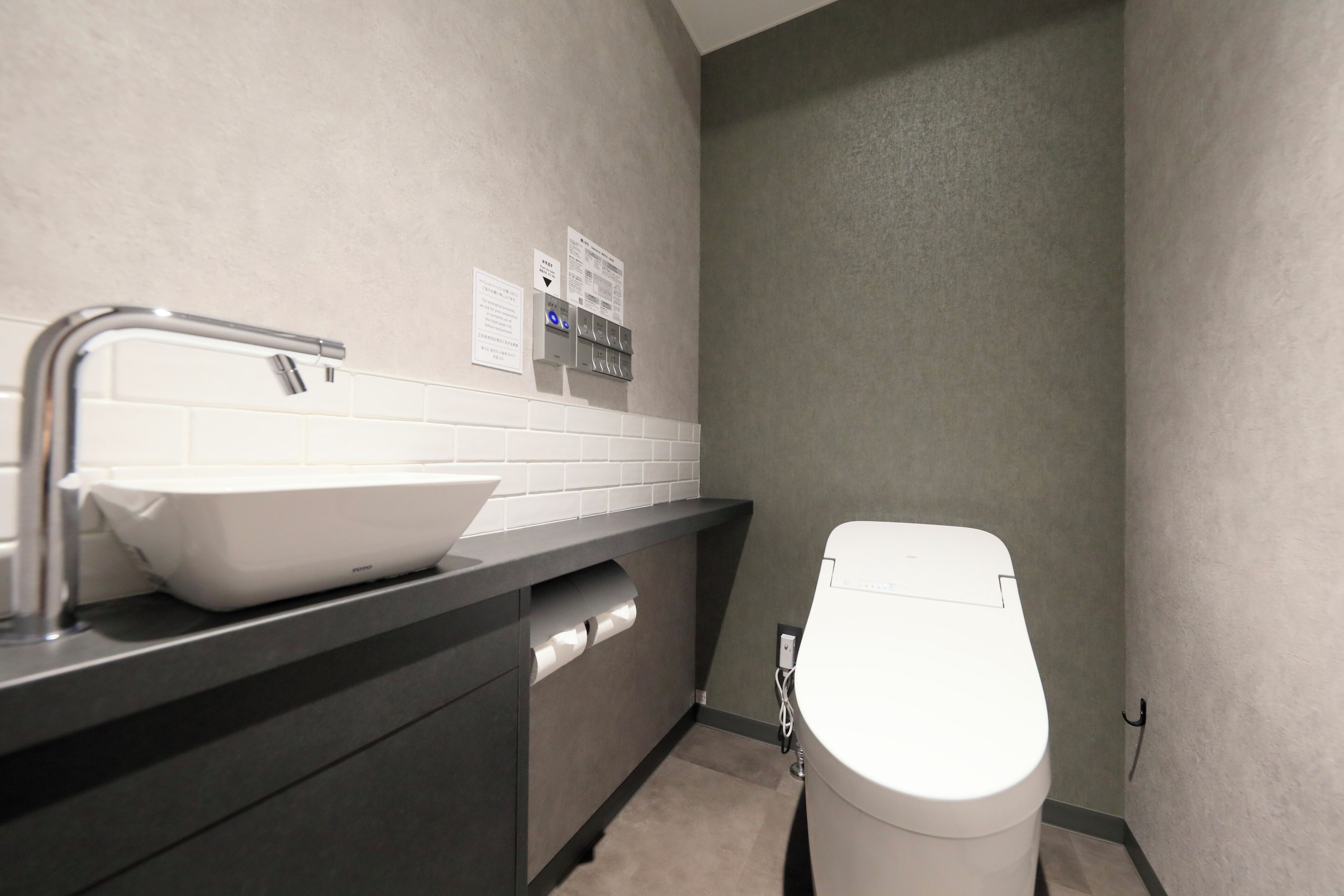 Un baño moderno con un lavamanos blanco, un inodoro y un dispensador de toallas.