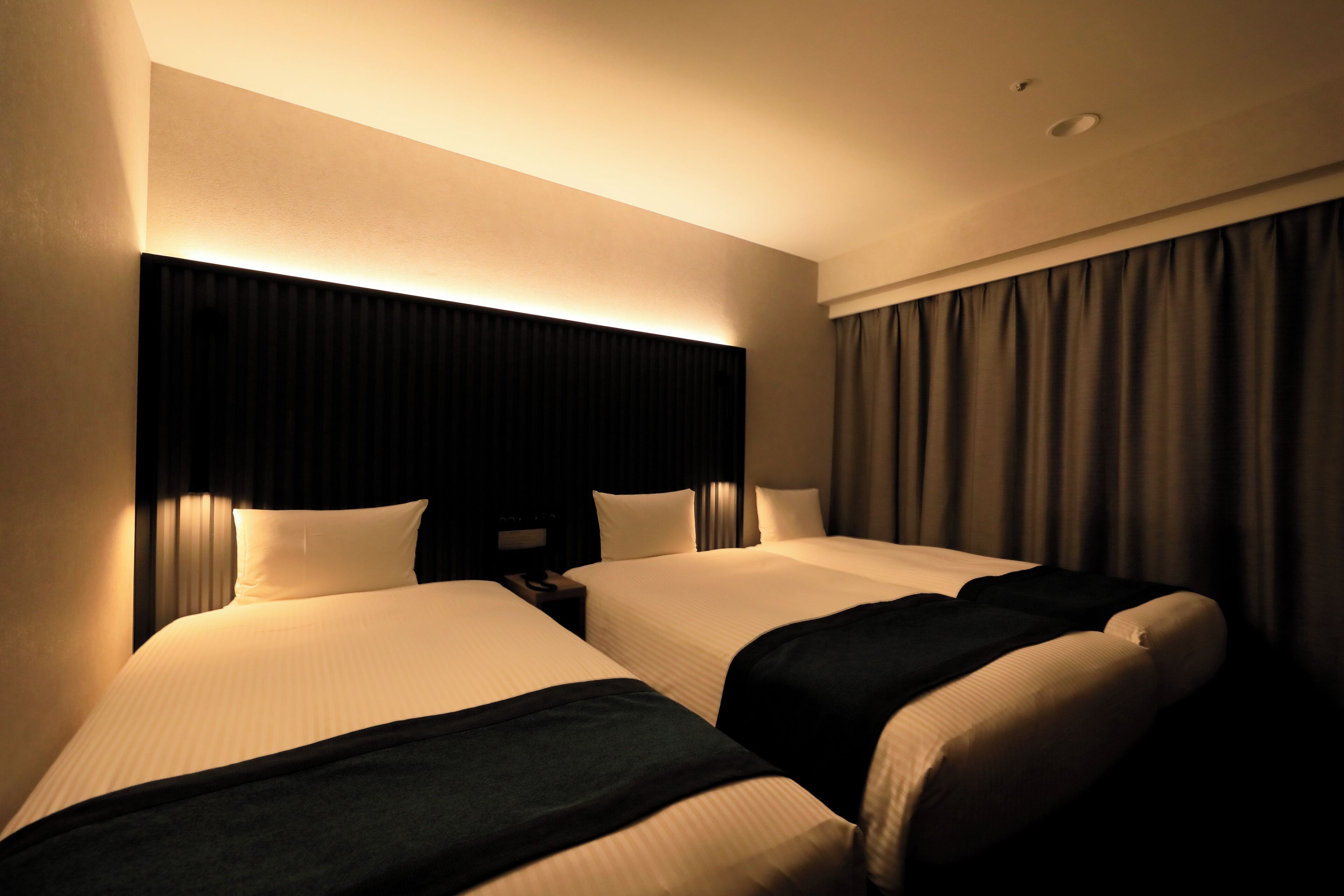A hotel room with two beds, a nightstand, and a large window with curtains.
