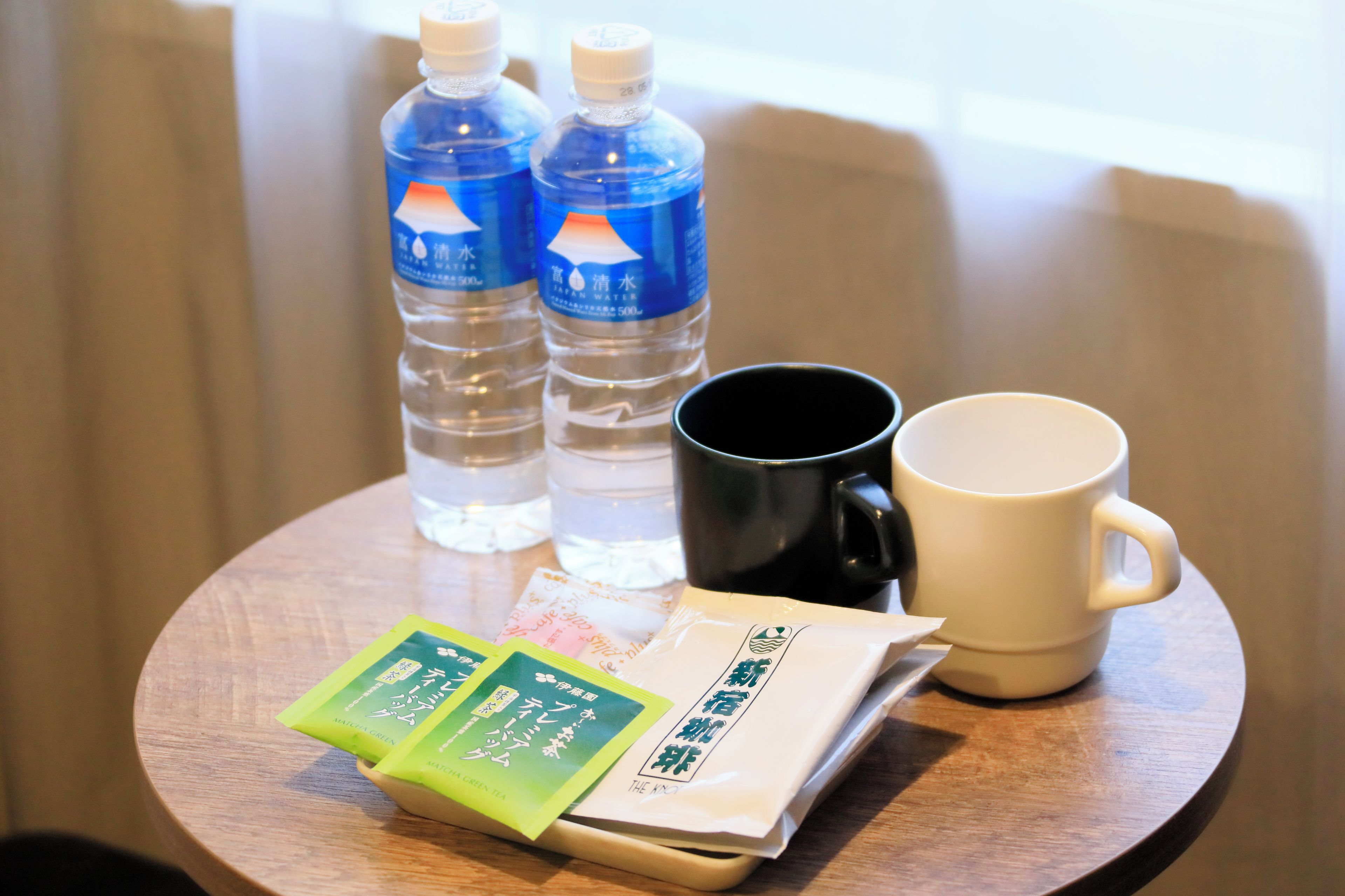 Une table en bois avec deux bouteilles d’eau, une tasse noire, une tasse blanche et deux sachets de thé.