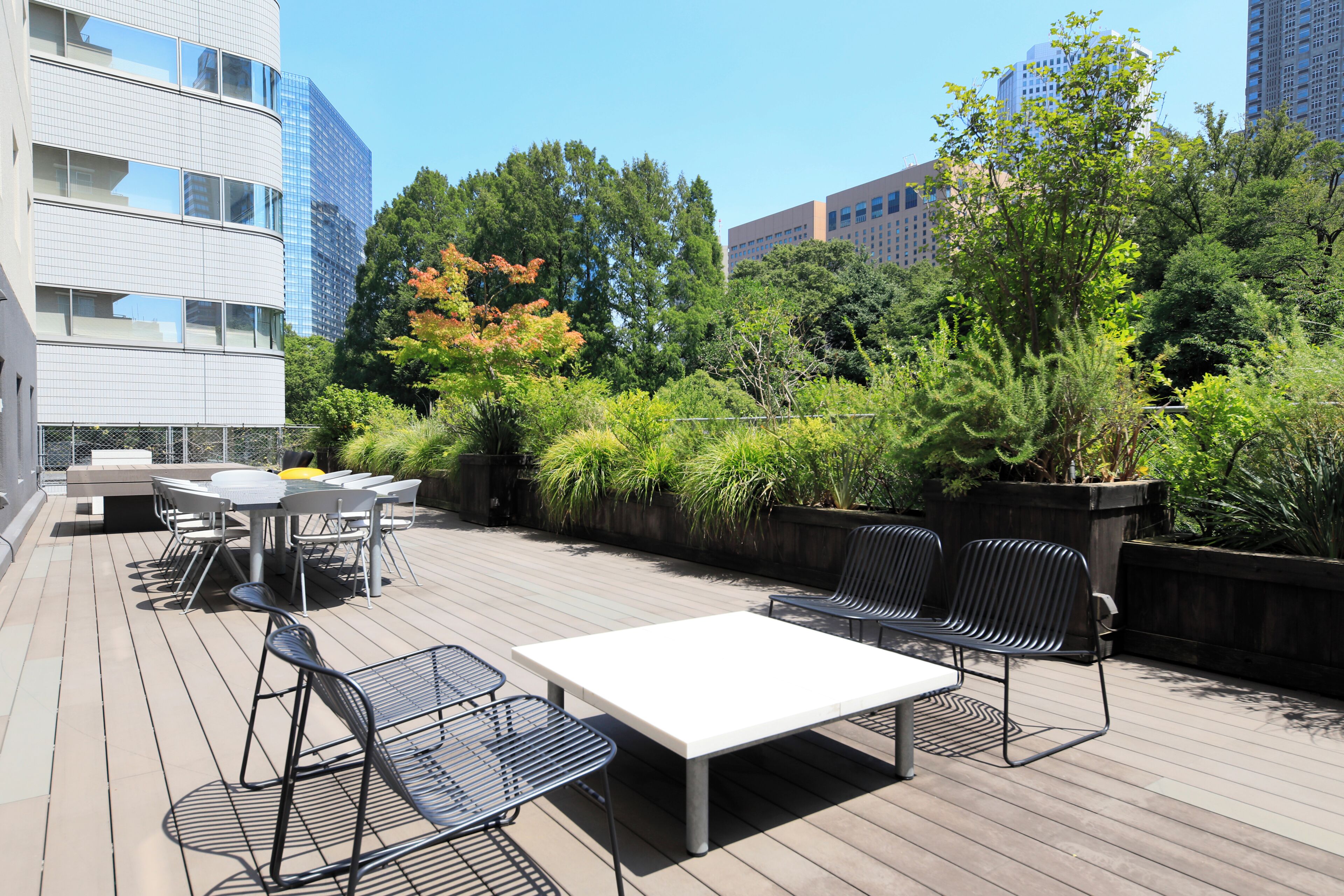 Terraza al aire libre con mesa y sillas, rodeada de vegetación y edificios.
