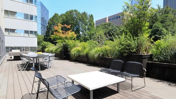 Terraza al aire libre con mesa y sillas, rodeada de vegetación y edificios.