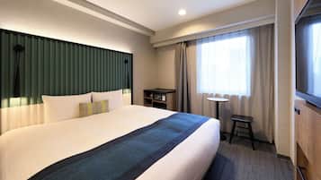 A hotel room with a large bed, a desk, a chair, a small table, a window with curtains, and a television.