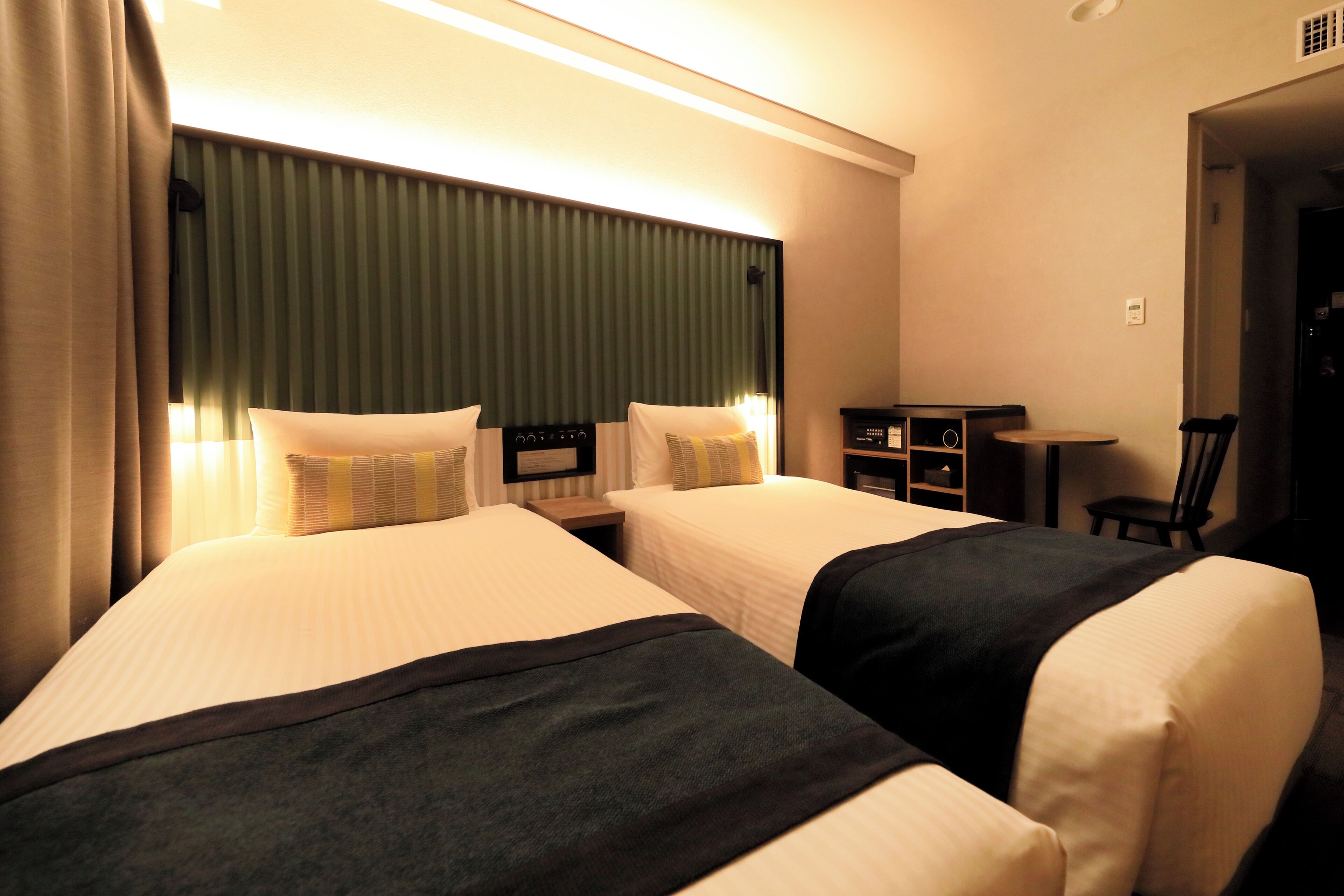 Hotellihuone, jossa on kaksi sänkyä, pieni pöytä ja tuoli.