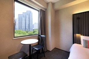 Una camera d'albergo con un letto, un tavolino, una sedia e una finestra con vista sulla città.