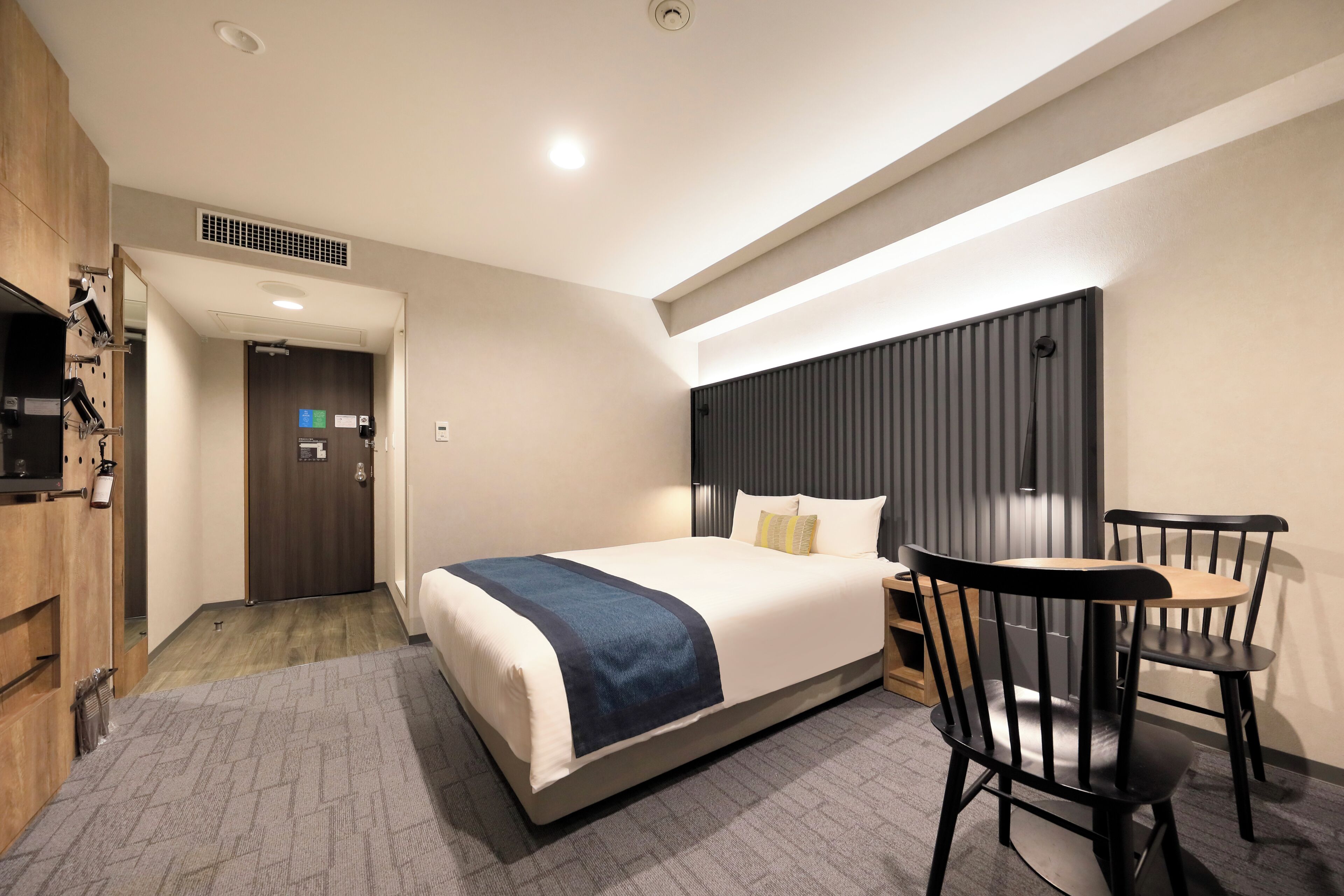 A hotel room with a bed, a desk, two chairs, a TV, and a bathroom with a shower.