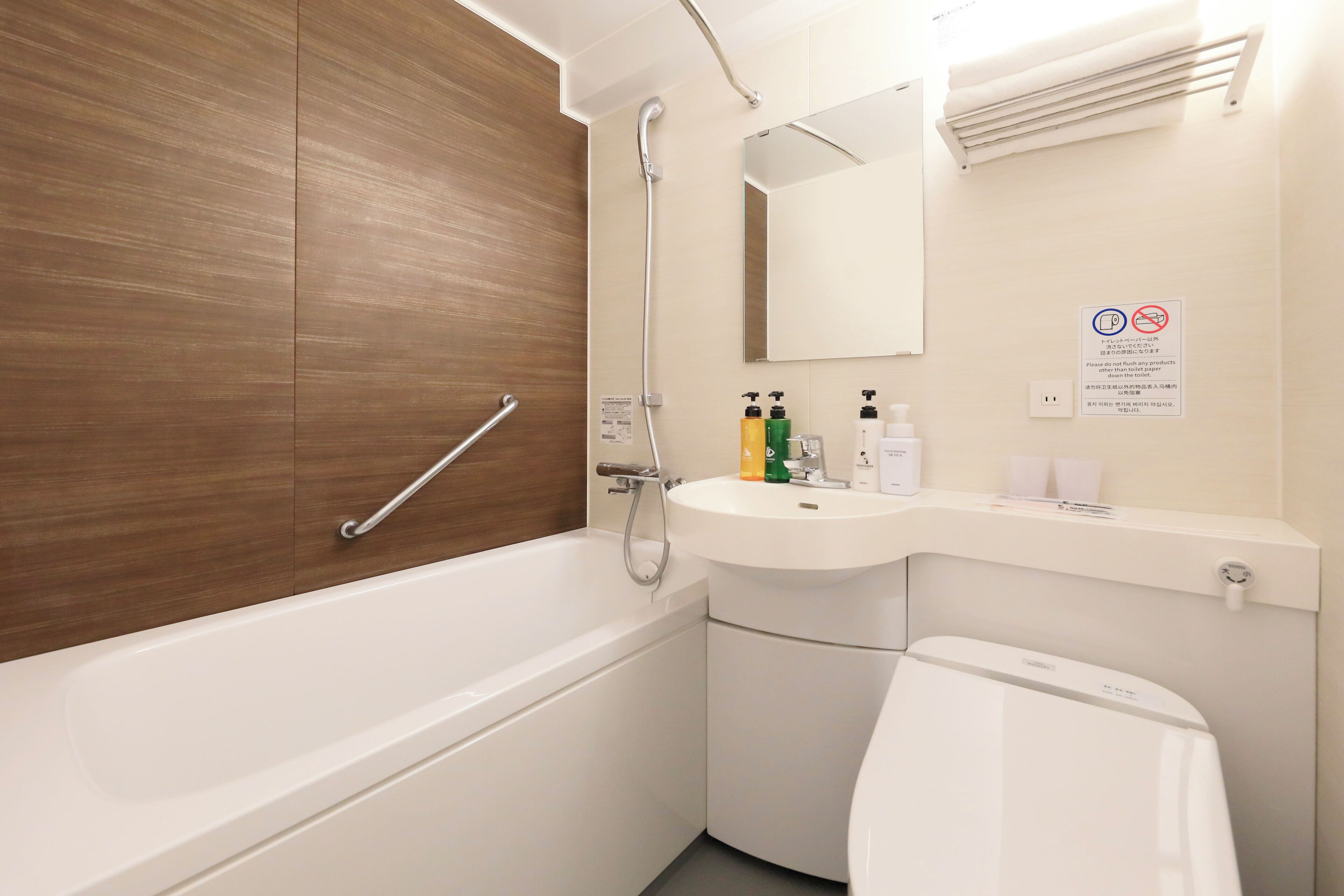 Une salle de bain moderne avec une baignoire, une douche, un meuble-lavabo et des toilettes. On trouve une barre d’appui sur la baignoire, un porte-serviettes au-dessus du lavabo et un miroir au mur.