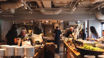 A busy kitchen with chefs preparing food, stainless steel appliances, and a high ceiling with exposed ductwork.