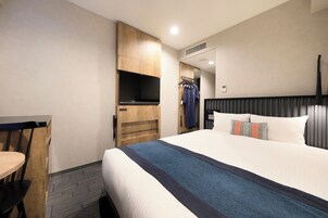 A hotel room with a bed, a desk, a chair, and a TV.