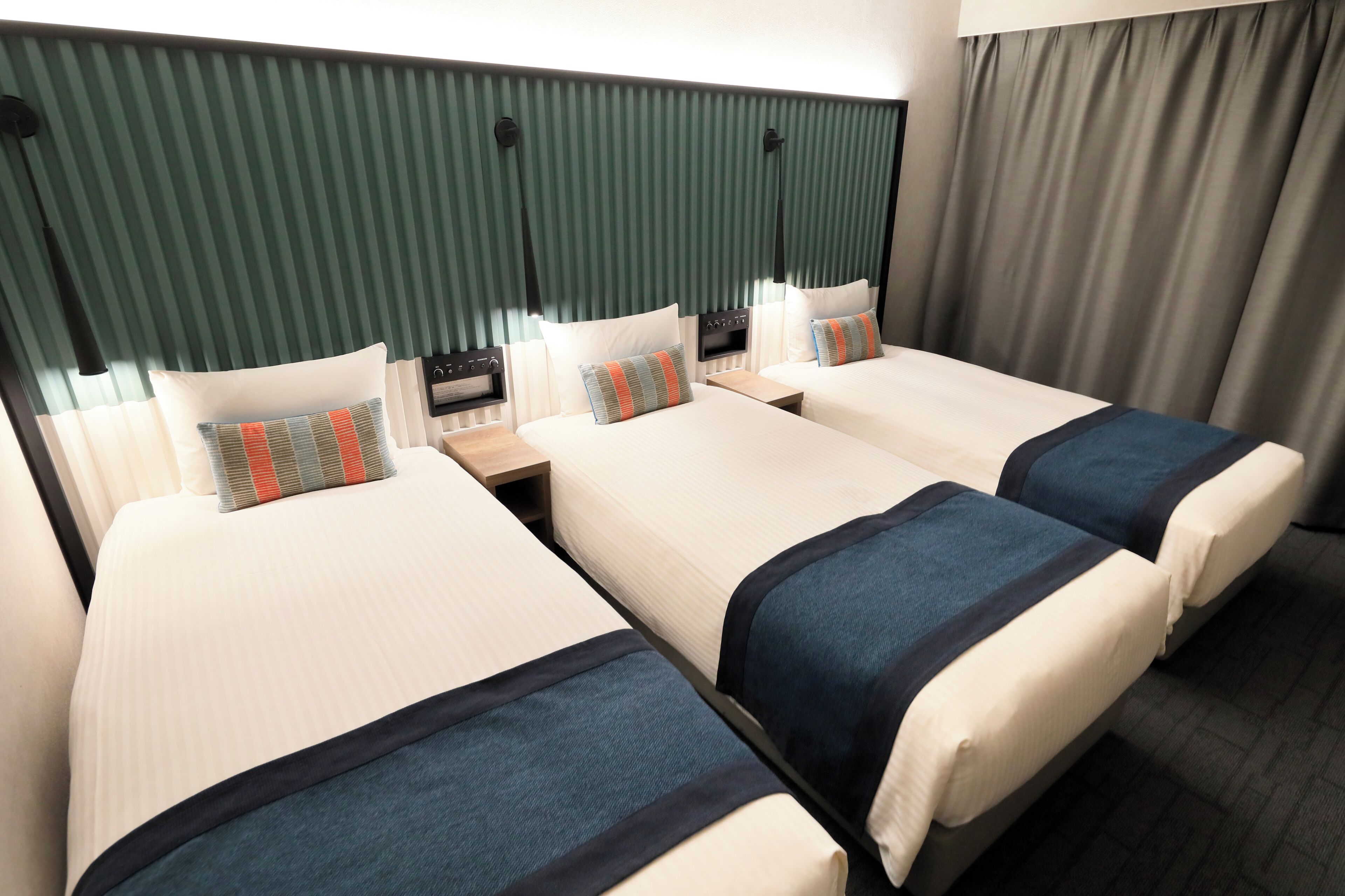 A hotel room with two beds, a nightstand, and a control panel.