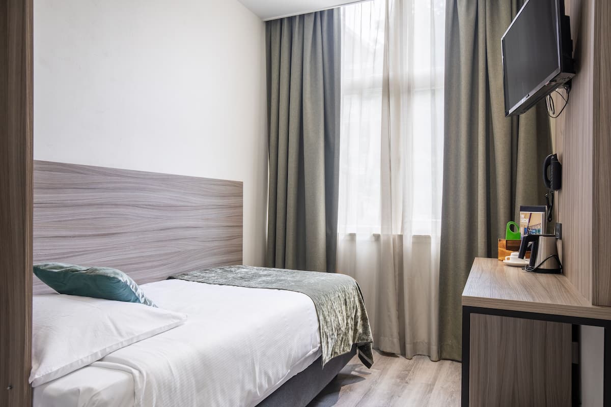 A hotel room with a bed, a desk, a TV, and a window with curtains.