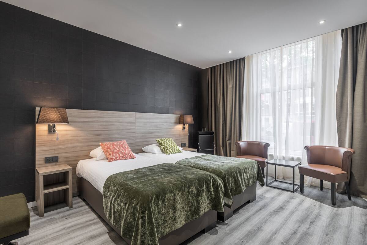 A modern hotel room with a large bed, two bedside tables, a nightstand, a sofa, and a chair.