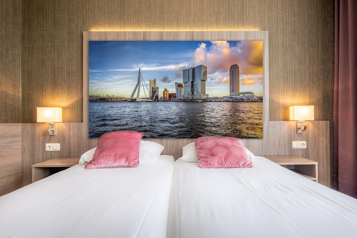 A hotel room with two beds, a cityscape painting on the wall, and two bedside lamps.