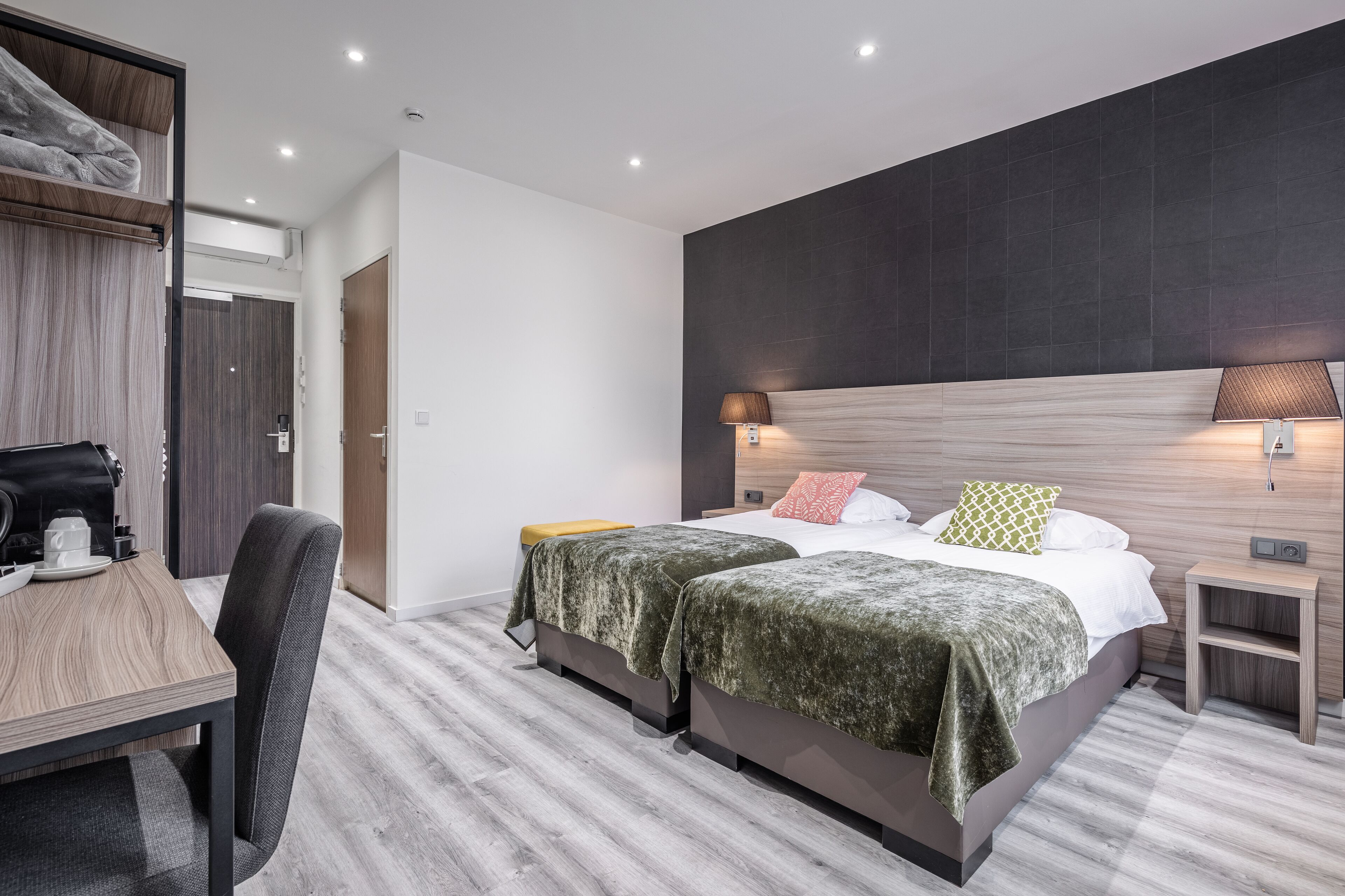 A modern hotel room with two beds, a desk with a chair, and a small bedside table.