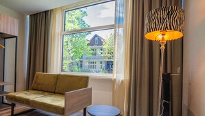 A room with a sofa, a small round table, a floor lamp, and a window with curtains.