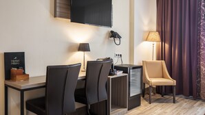 A hotel room with a flat-screen TV, a desk with a lamp, a telephone, and a chair.