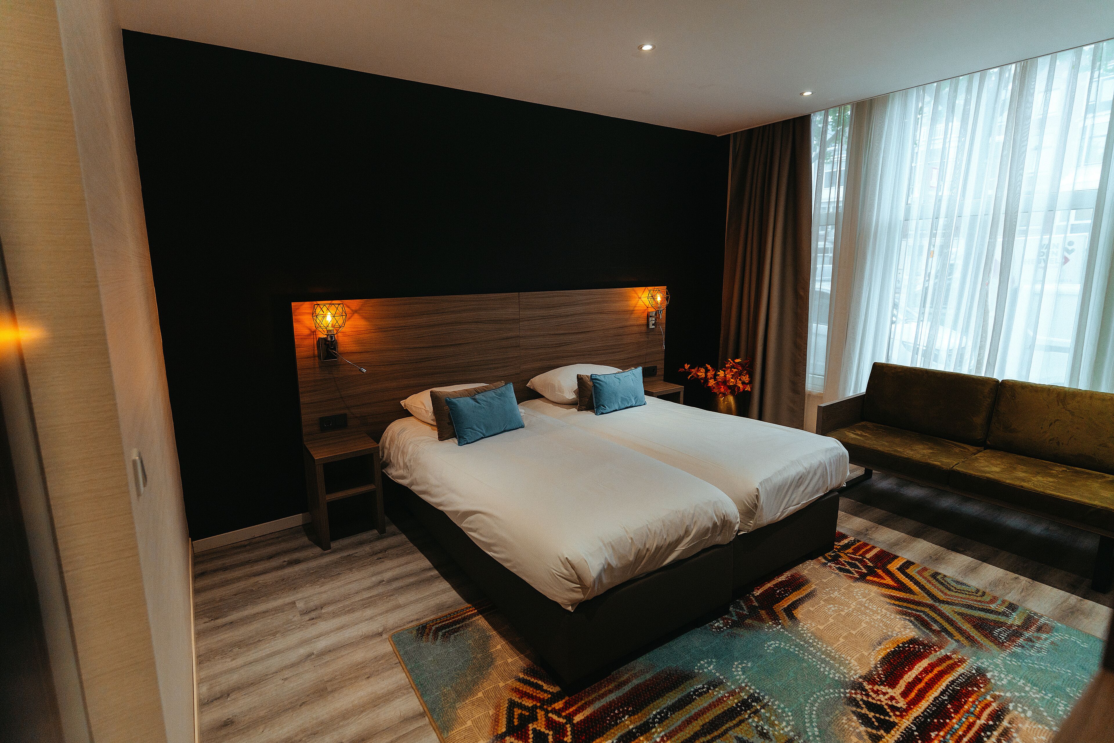 A modern hotel room with a large bed, a sofa, and a nightstand.