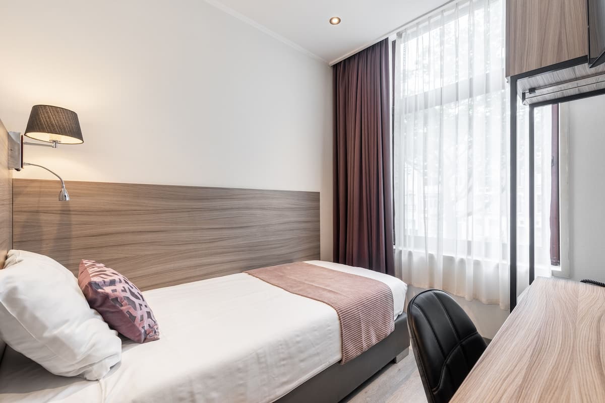 A hotel room with a bed, a desk, and a lamp.