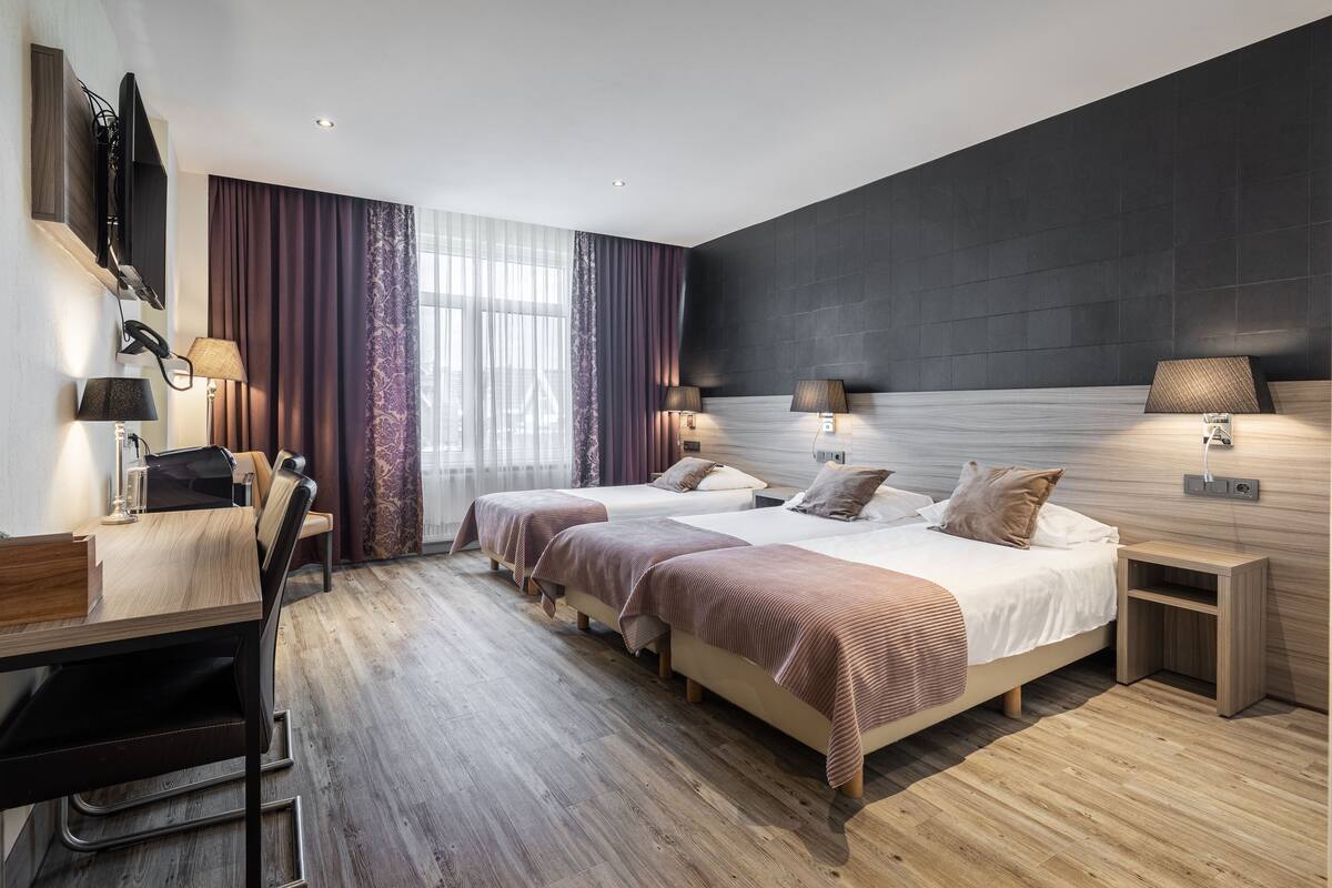 A modern hotel room with two beds, a desk with a chair, and a TV mounted on the wall.