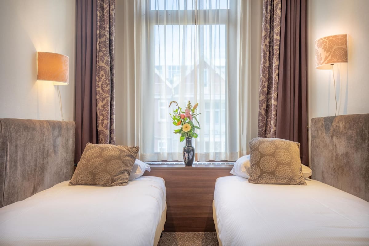 A hotel room with two beds, a vase with flowers, and curtains.