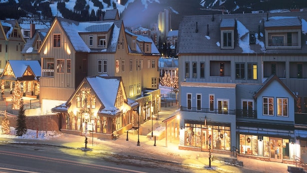 Un pueblo nevado al anochecer, con edificios iluminados y una vista despejada de las montañas.