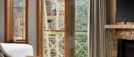 Una habitación con cama, chimenea, ventana grande con vista a árboles y puerta corrediza de vidrio.