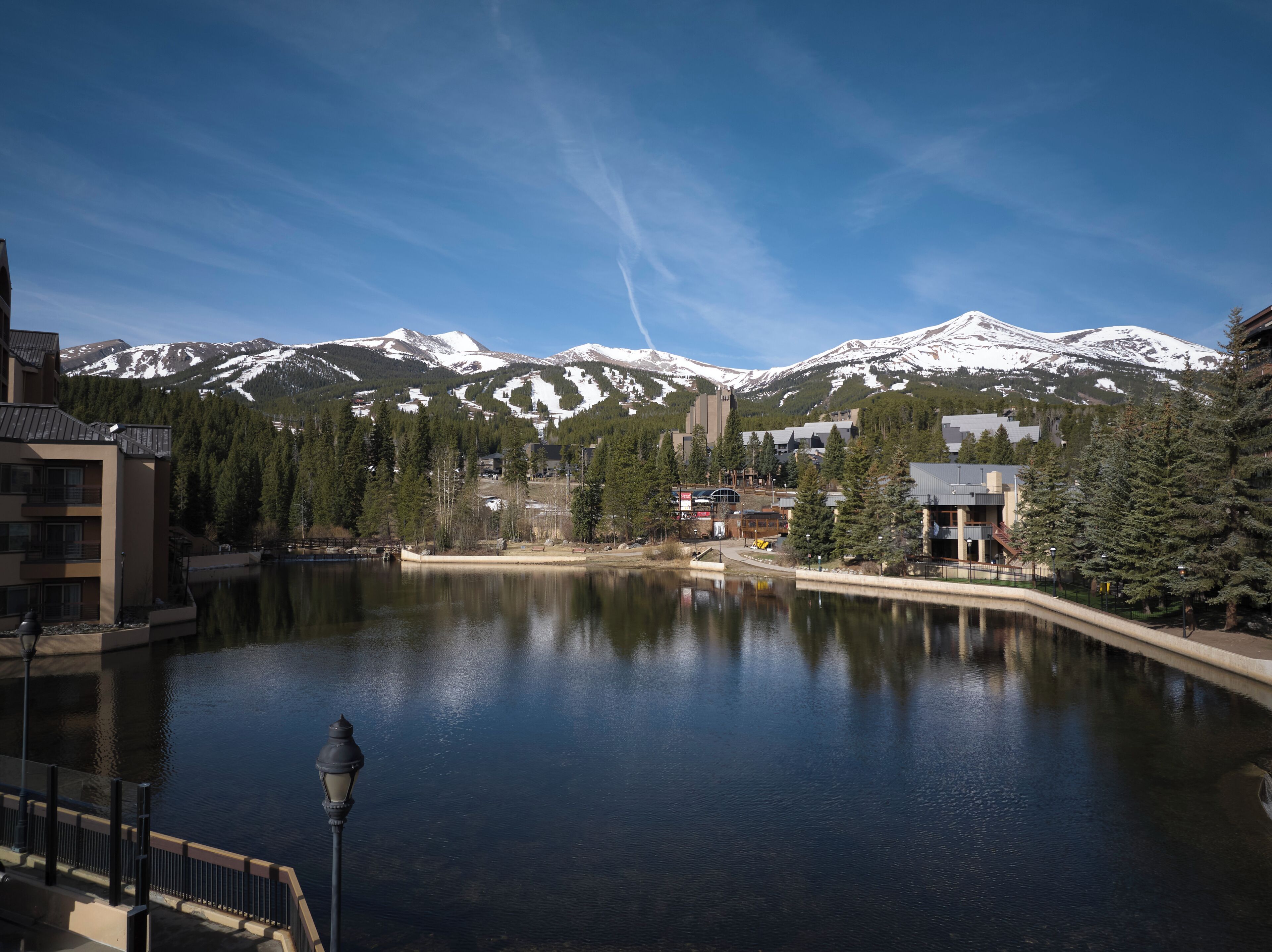 Un lac avec une chaîne de montagnes en arrière-plan, des bâtiments et un lampadaire.