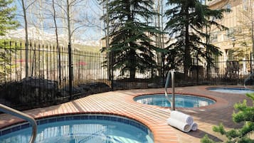 A pool area with multiple hot tubs, surrounded by a brick patio and a metal fence.