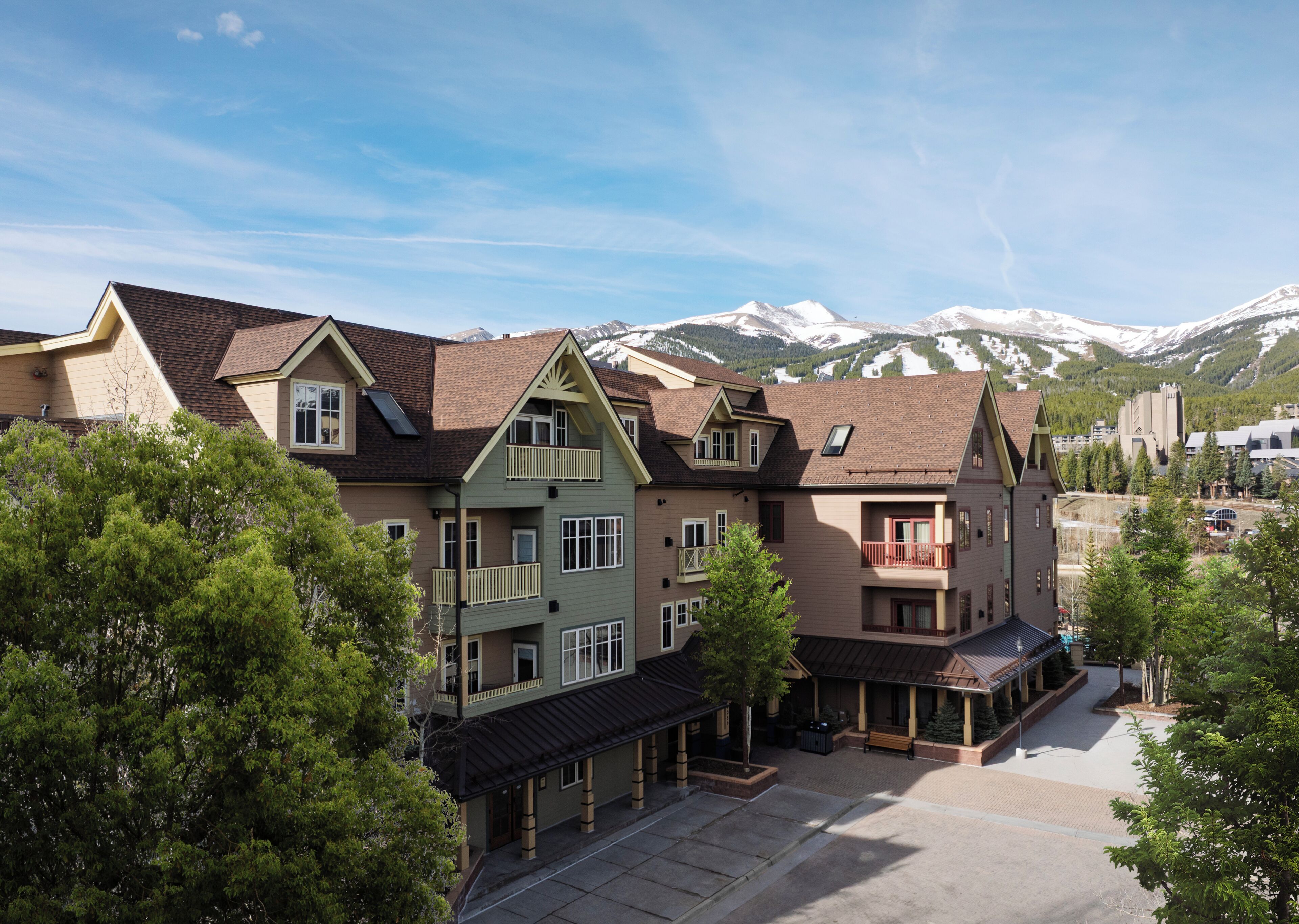 A multi-story hotel with balconies, a covered outdoor seating area, and a view of snow-capped mountains.