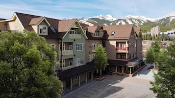 A multi-story hotel with balconies, a covered outdoor seating area, and a view of snow-capped mountains.