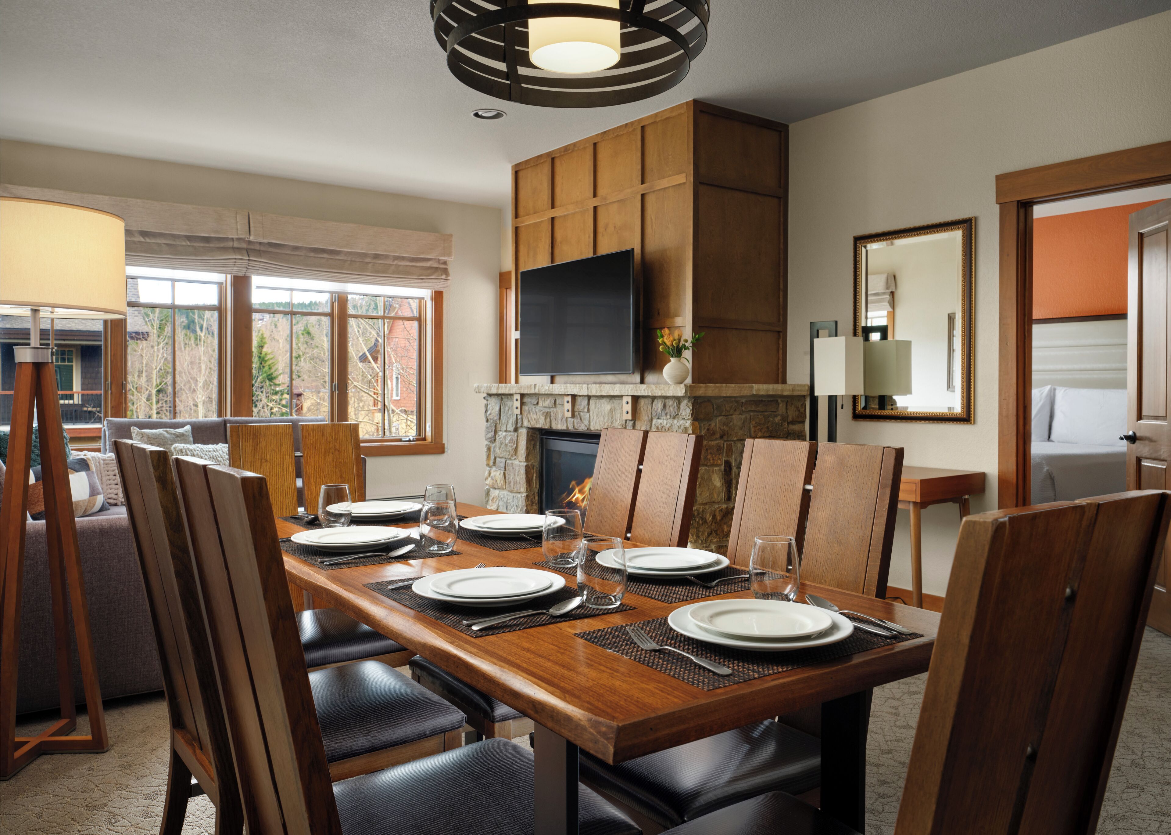 Un espace repas avec une longue table en bois, dressée pour six personnes, entourée de chaises, agrémenté d’une cheminée et d’un téléviseur fixé au-dessus.