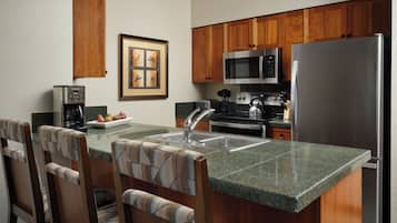 Una cocina con armarios de madera, un refrigerador de acero inoxidable, un microondas, una cafetera y un lavabo.