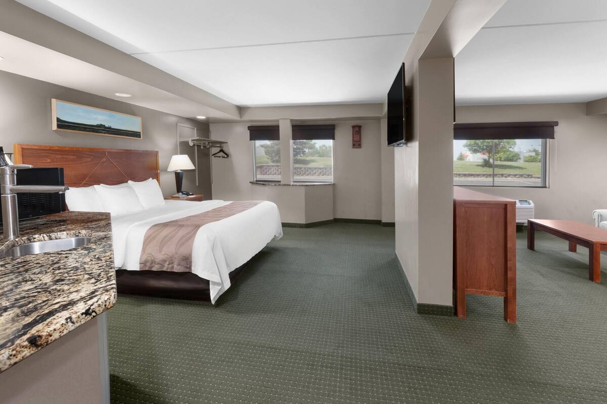 A hotel room with a bed, a desk, a chair, a TV, a painting, and a window.