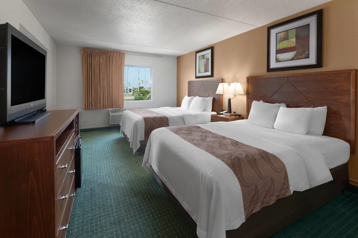 A hotel room with two beds, a TV, a desk, and a window with curtains.