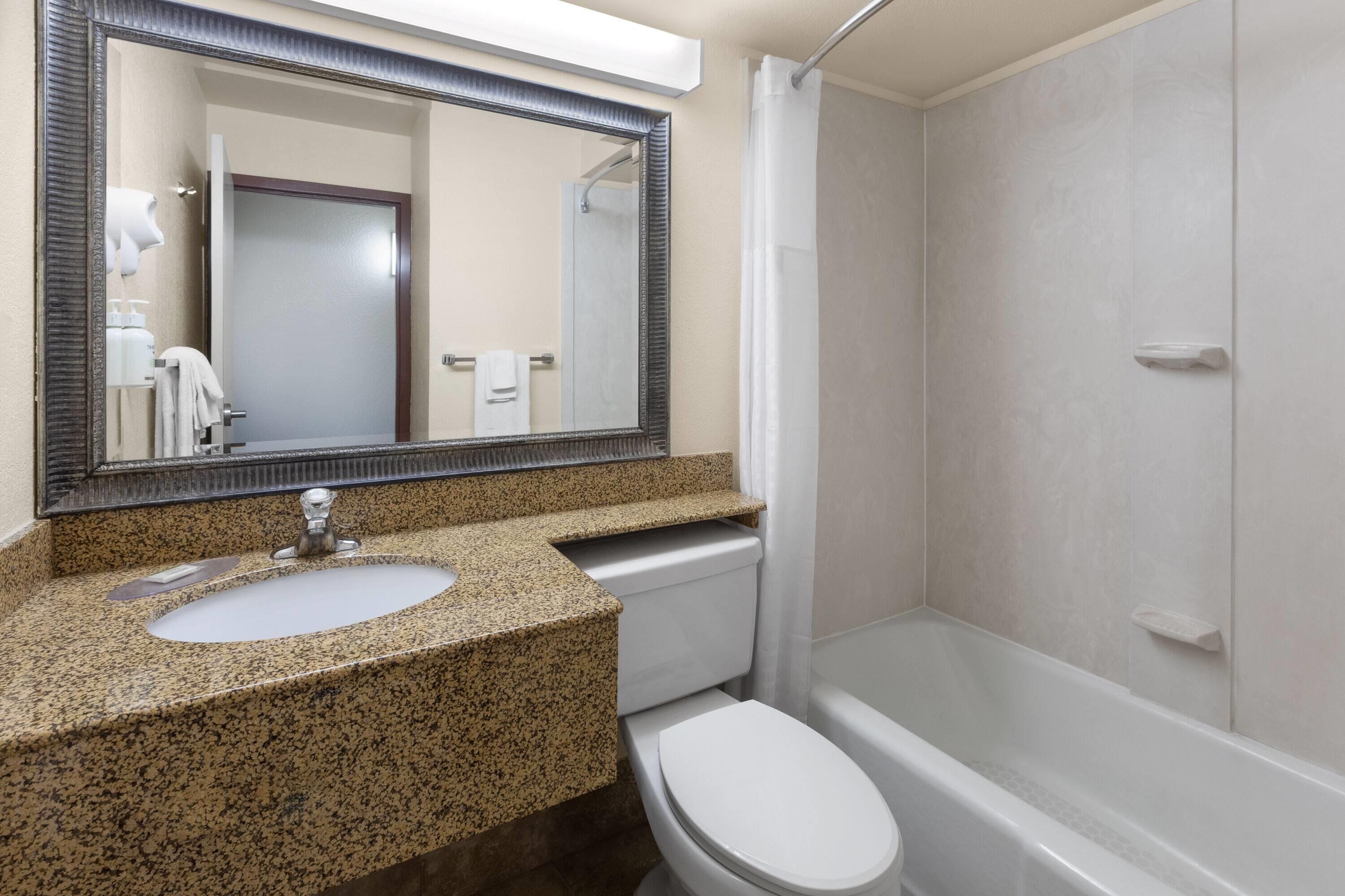 A bathroom with a granite countertop sink, a white toilet, and a bathtub.