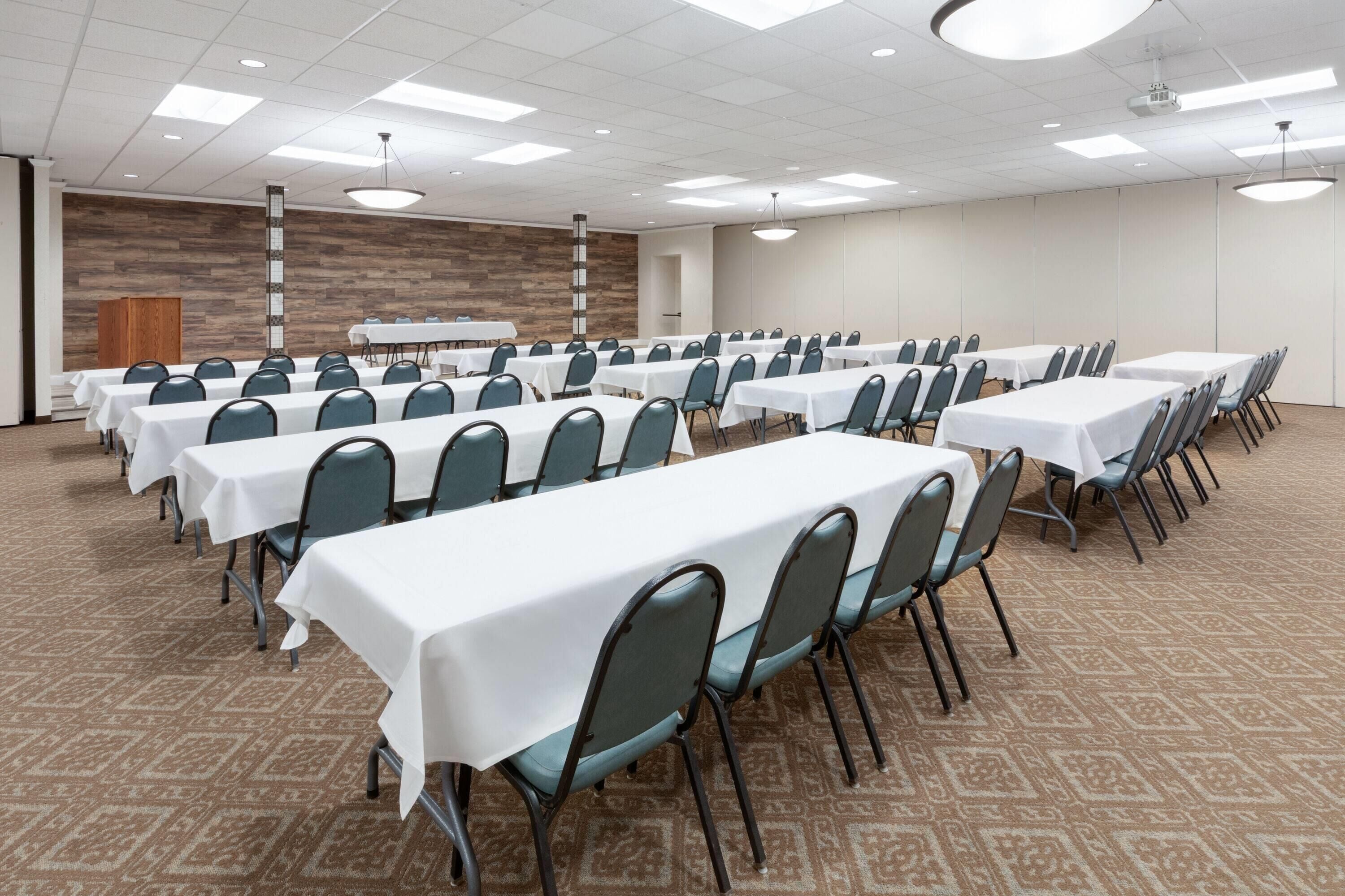 A conference room with multiple tables and chairs, a wooden accent wall, and a carpeted floor.