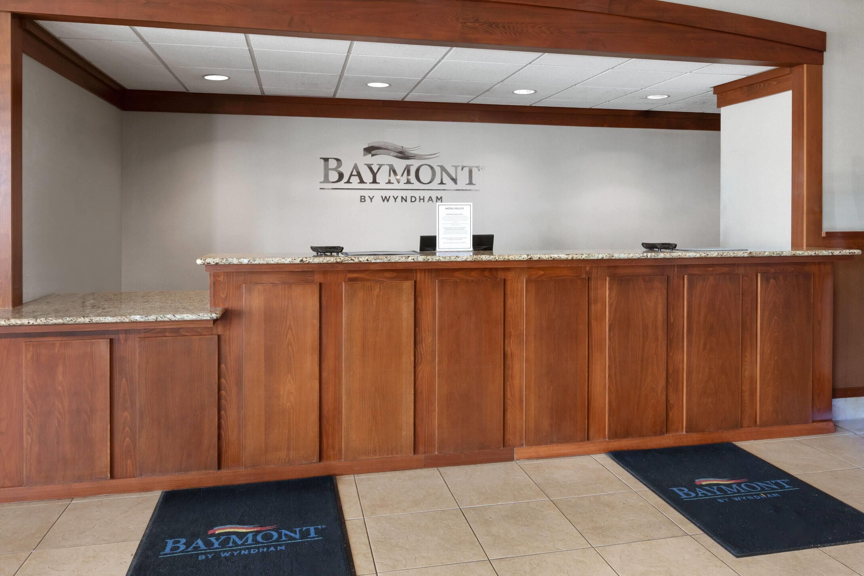 A reception desk with a wooden finish, a sign above it, and two doormats on the floor.