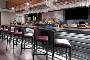 A bar area with multiple red bar stools, a bar counter with various bottles and a cash register, and a large screen above the bar. - Baymont by Wyndham Jamestown Conference Center & Water Park (Jamestown)