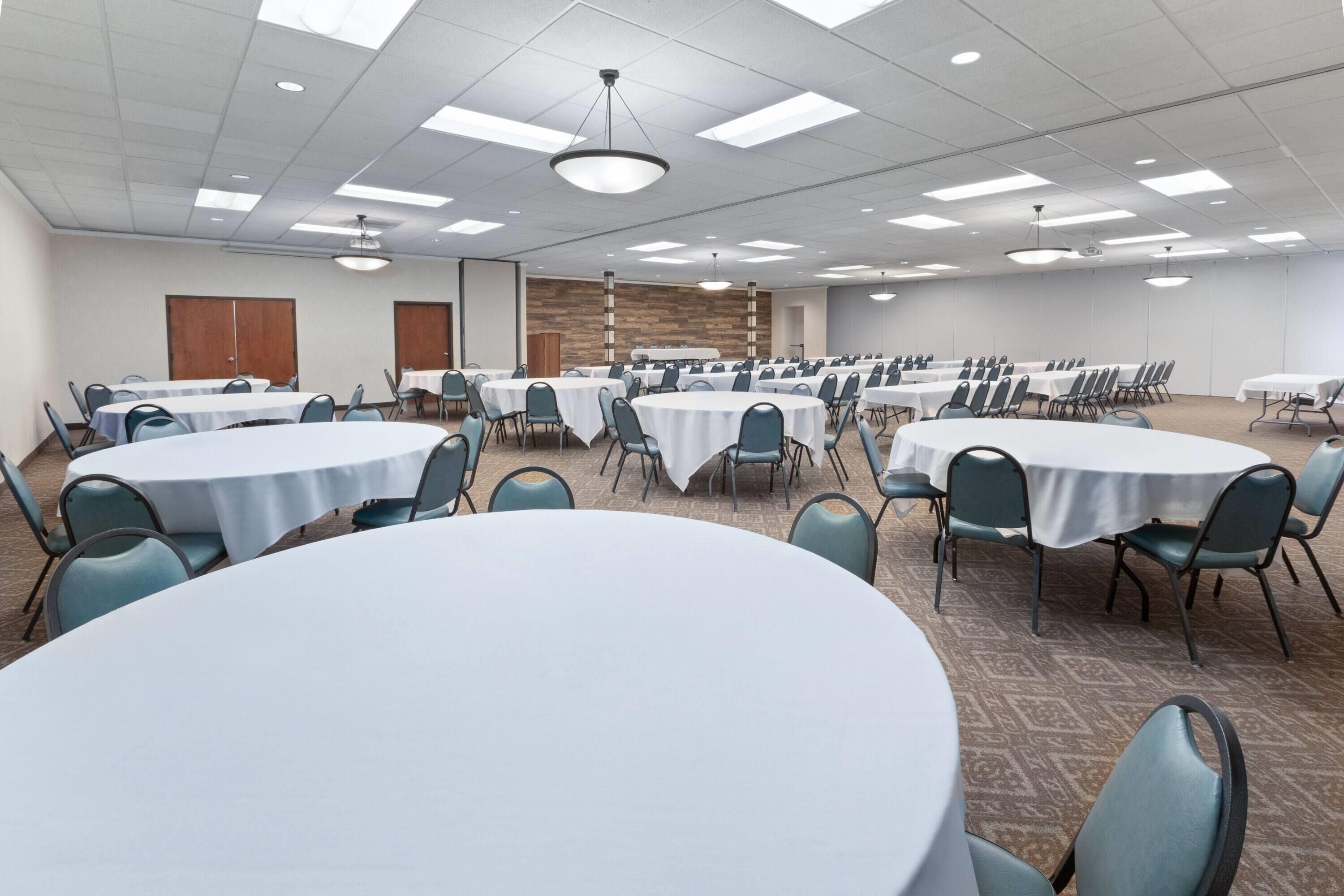 A conference room with multiple round tables, chairs, and a wooden accent wall.