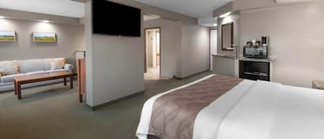 A hotel room with a large bed, a sofa, a TV, and a kitchenette.