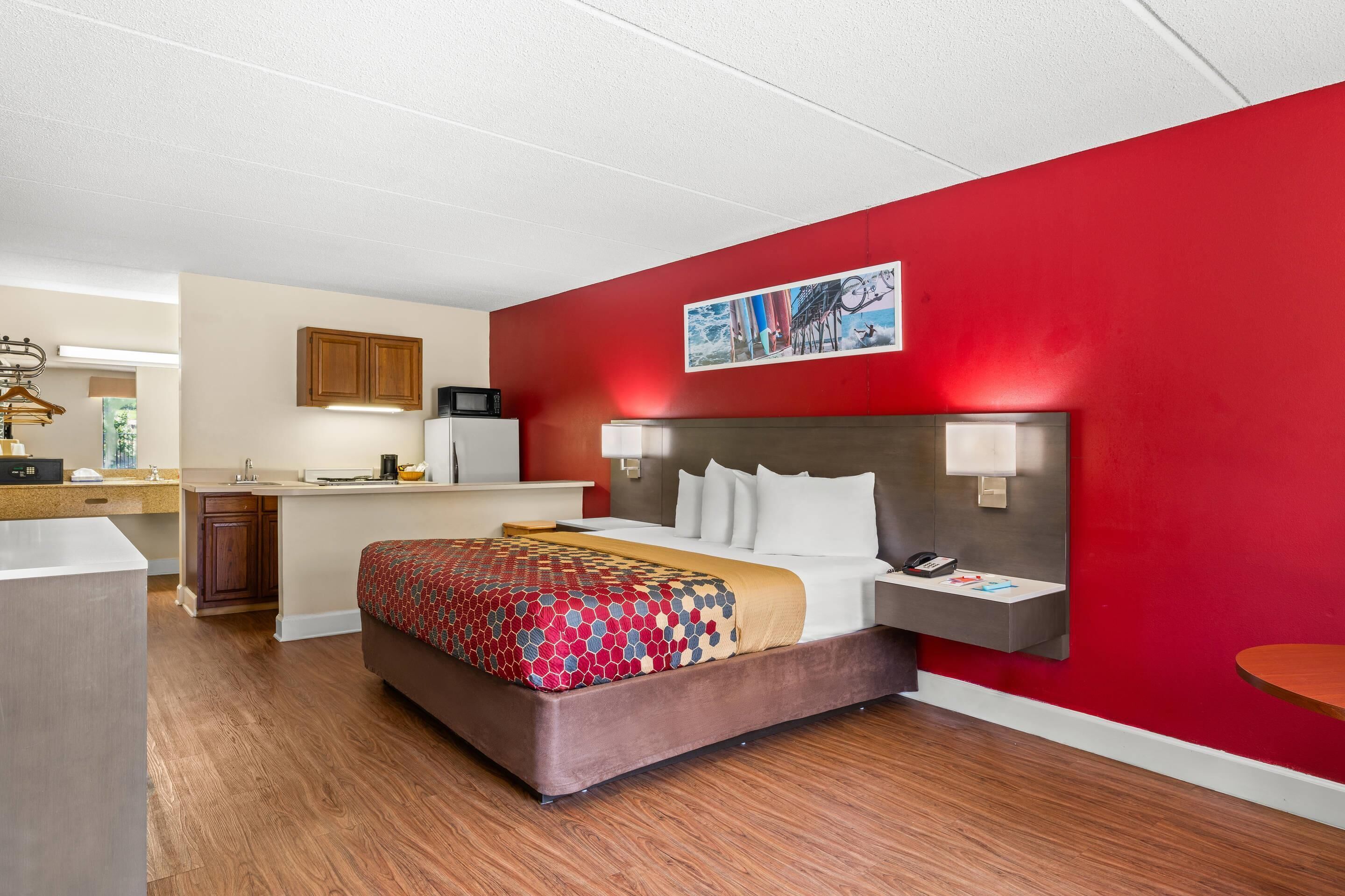 Une chambre d’hôtel avec un lit, un bureau, un four à micro-ondes et un mur rouge.