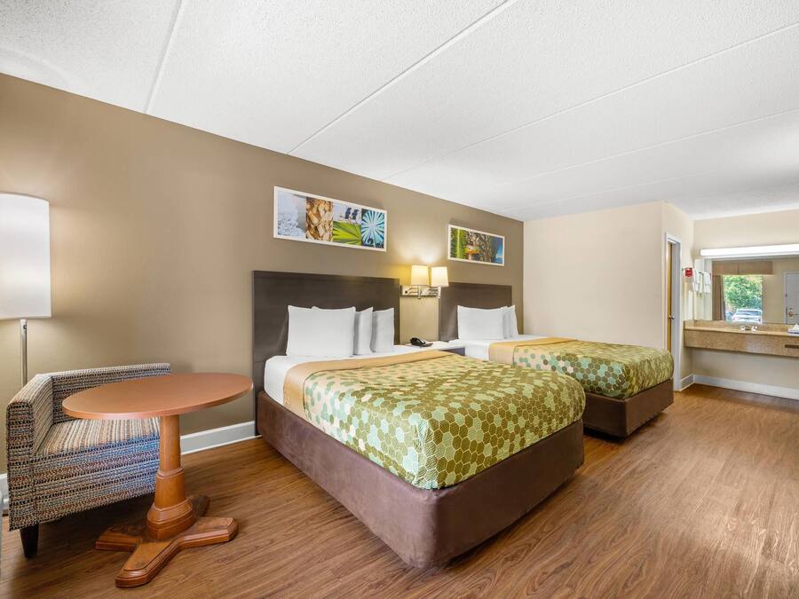 A hotel room with two beds, a small round table, and a chair. There is a desk with a mirror and a window.